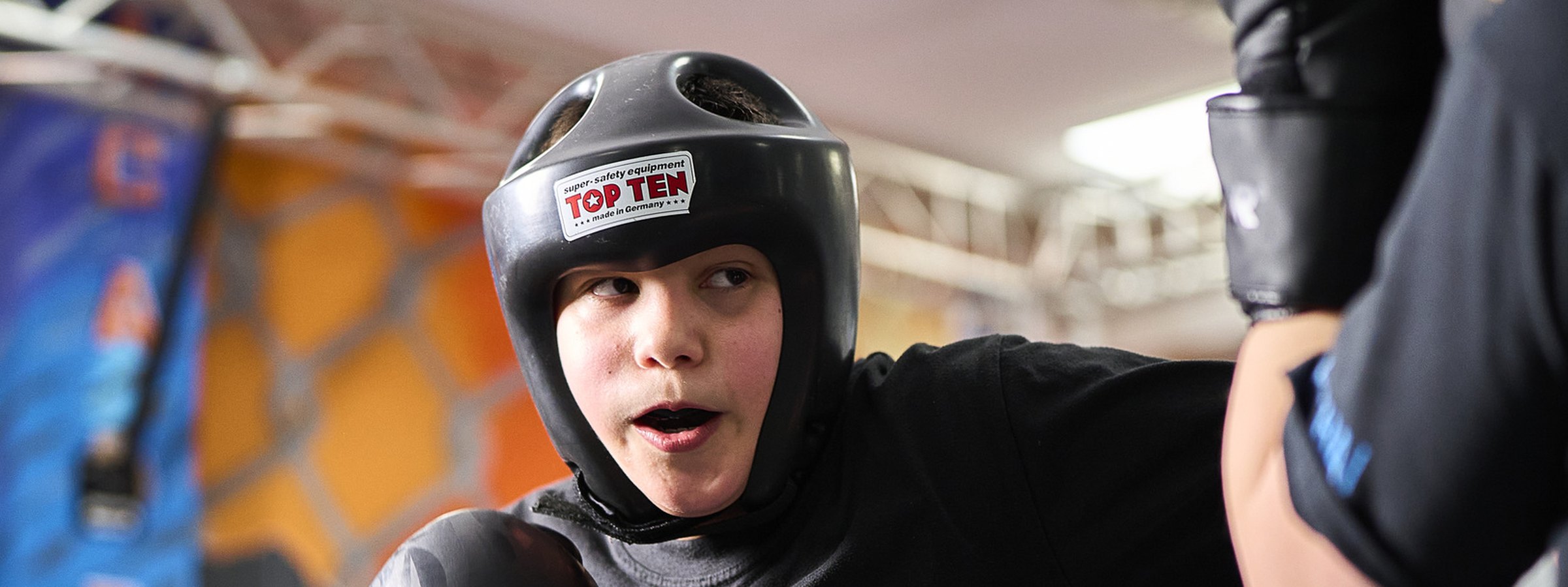 Ein Junge mit Kopfschutz im Ring, gegenüber die gehaltene Pratze — Halle Lahr, August 2026.