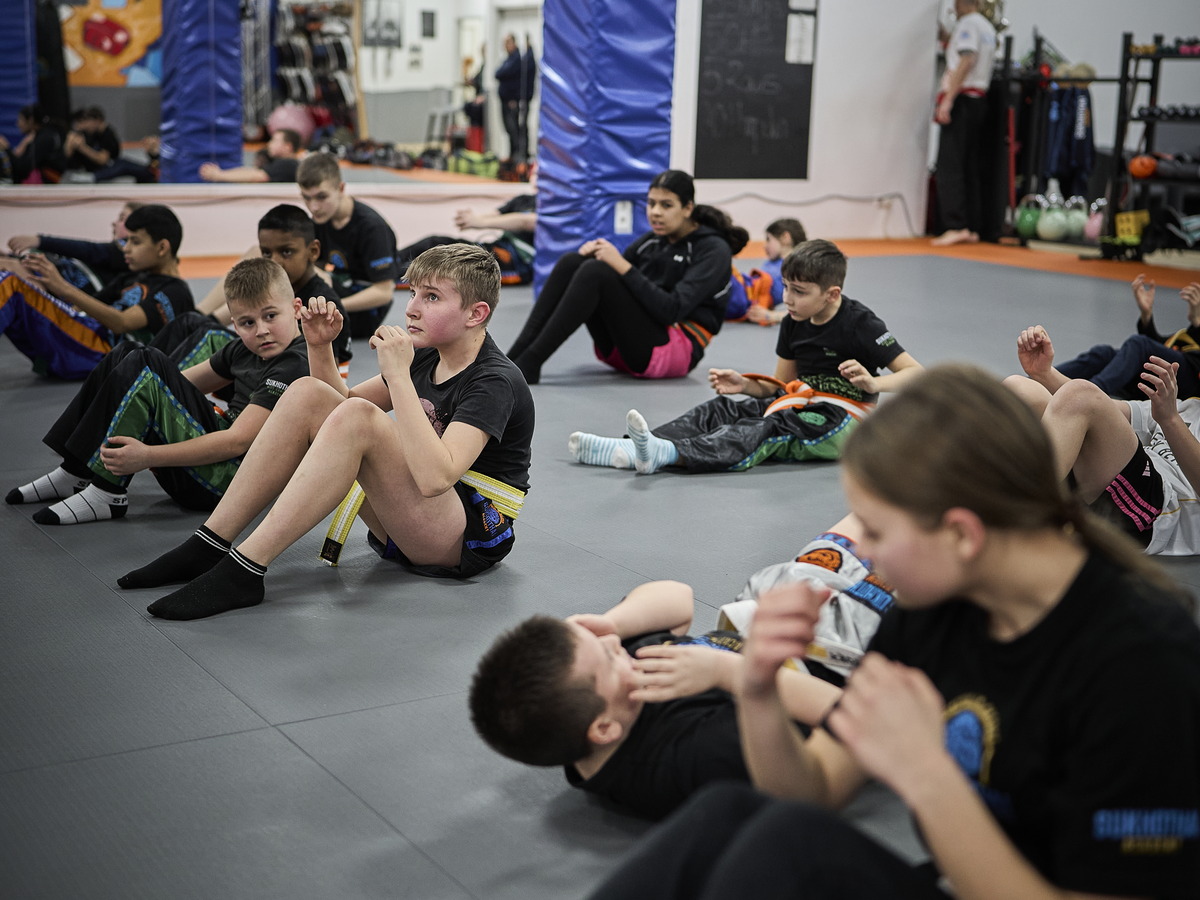 Ein Mädchen hält einem Jungen bei den Sit-ups die Füße, im Hintergrund trainiert die Gruppe.